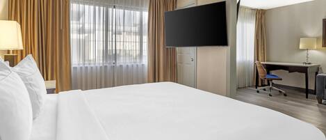 Une chambre d’hôtel avec un grand lit, un bureau, une chaise, une télévision et des rideaux.