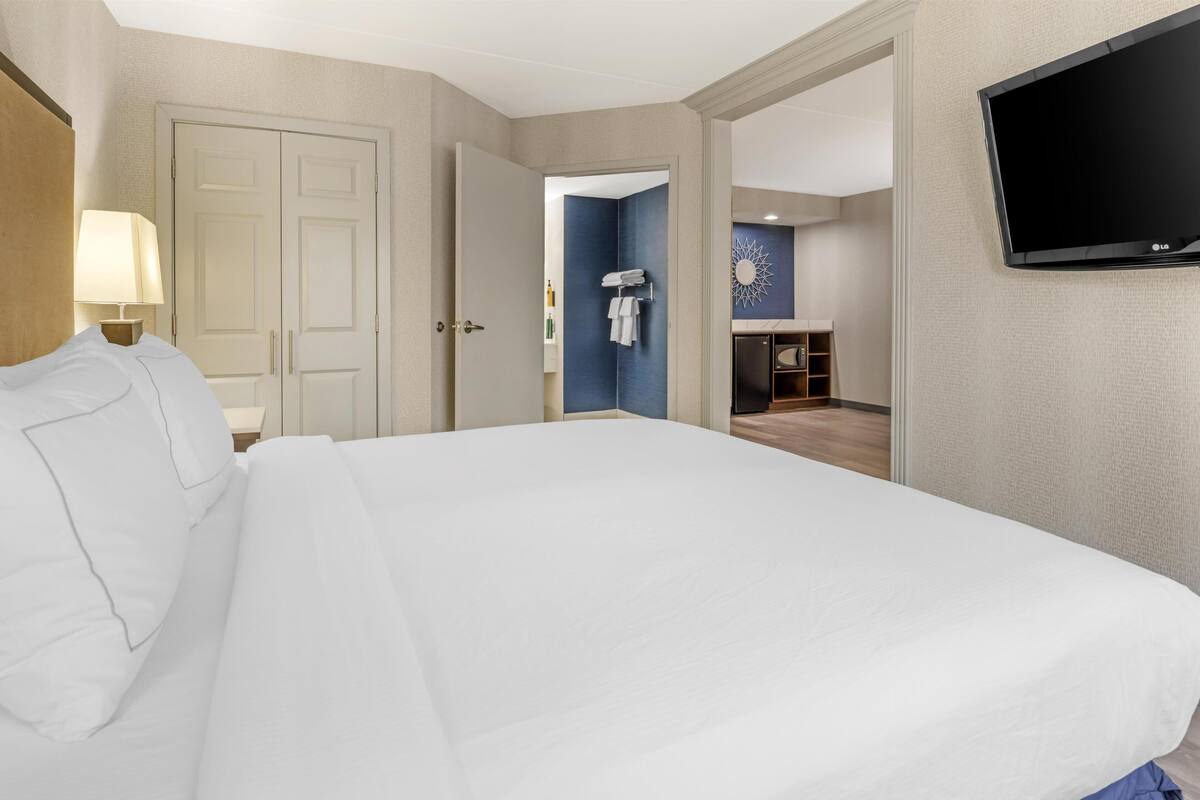 Ein Hotelzimmer mit Bett, Fernseher, einer Tür und einem im Hintergrund sichtbaren Badezimmer.