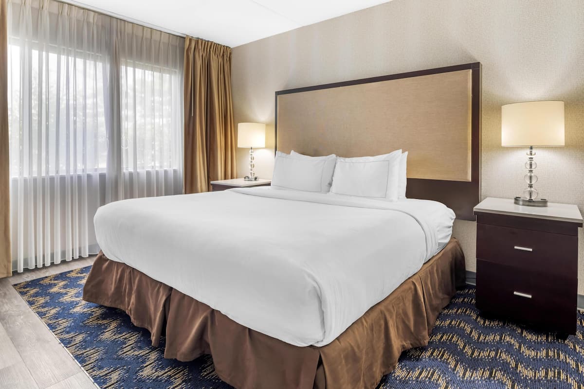 Ein Hotelzimmer mit einem großen Bett, zwei Nachttischen, einer Kopfteil und einem Vorhangfenster.