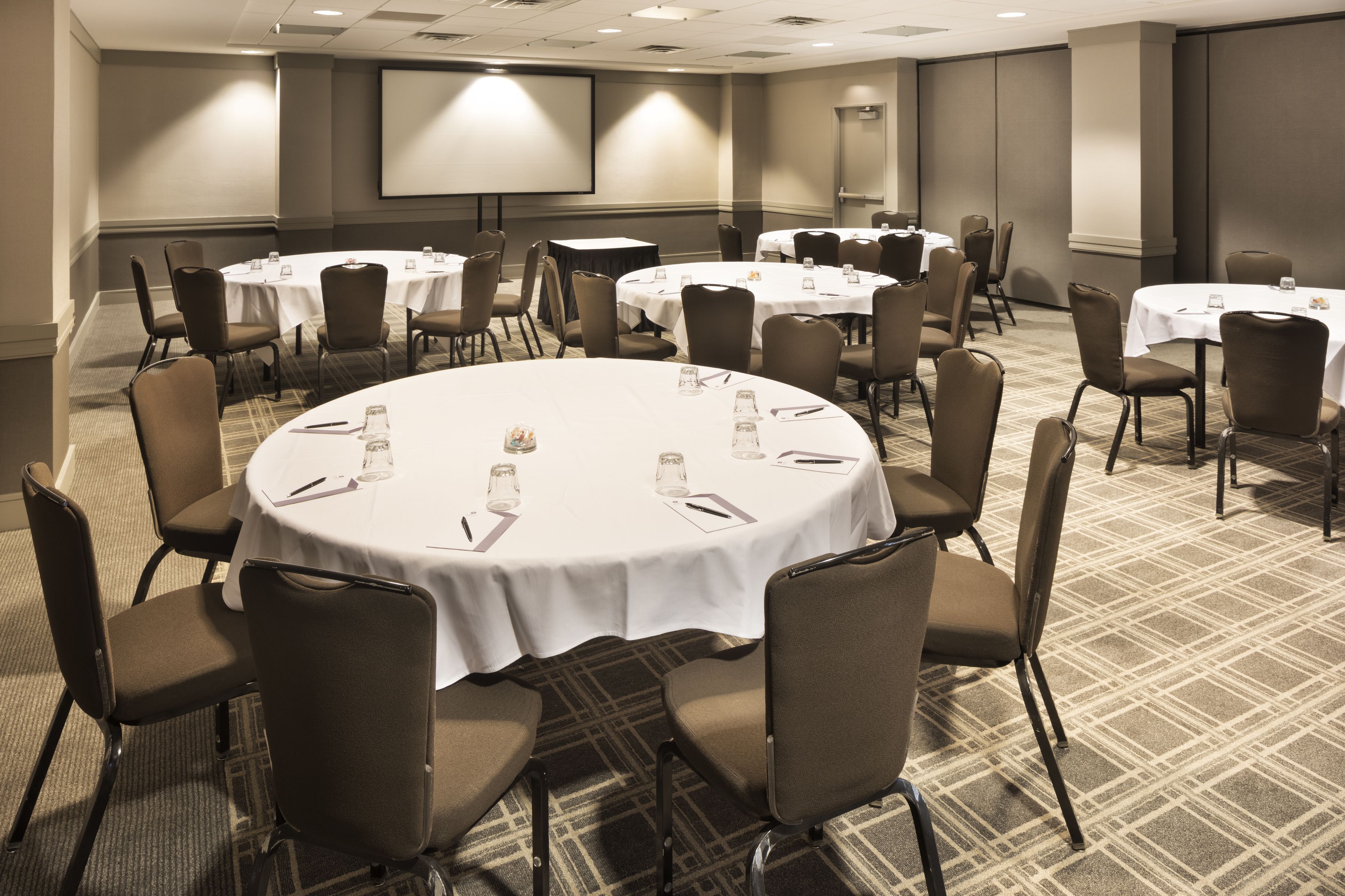 A conference room with round tables, chairs, and a projector screen.