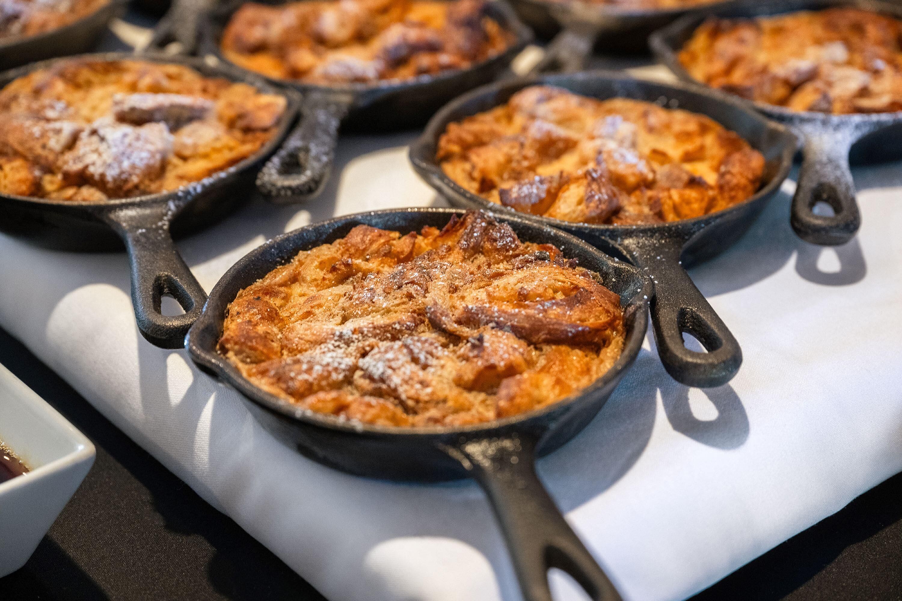 A series of cast iron skillets filled with baked goods, likely bread or pastries, arranged on a table.