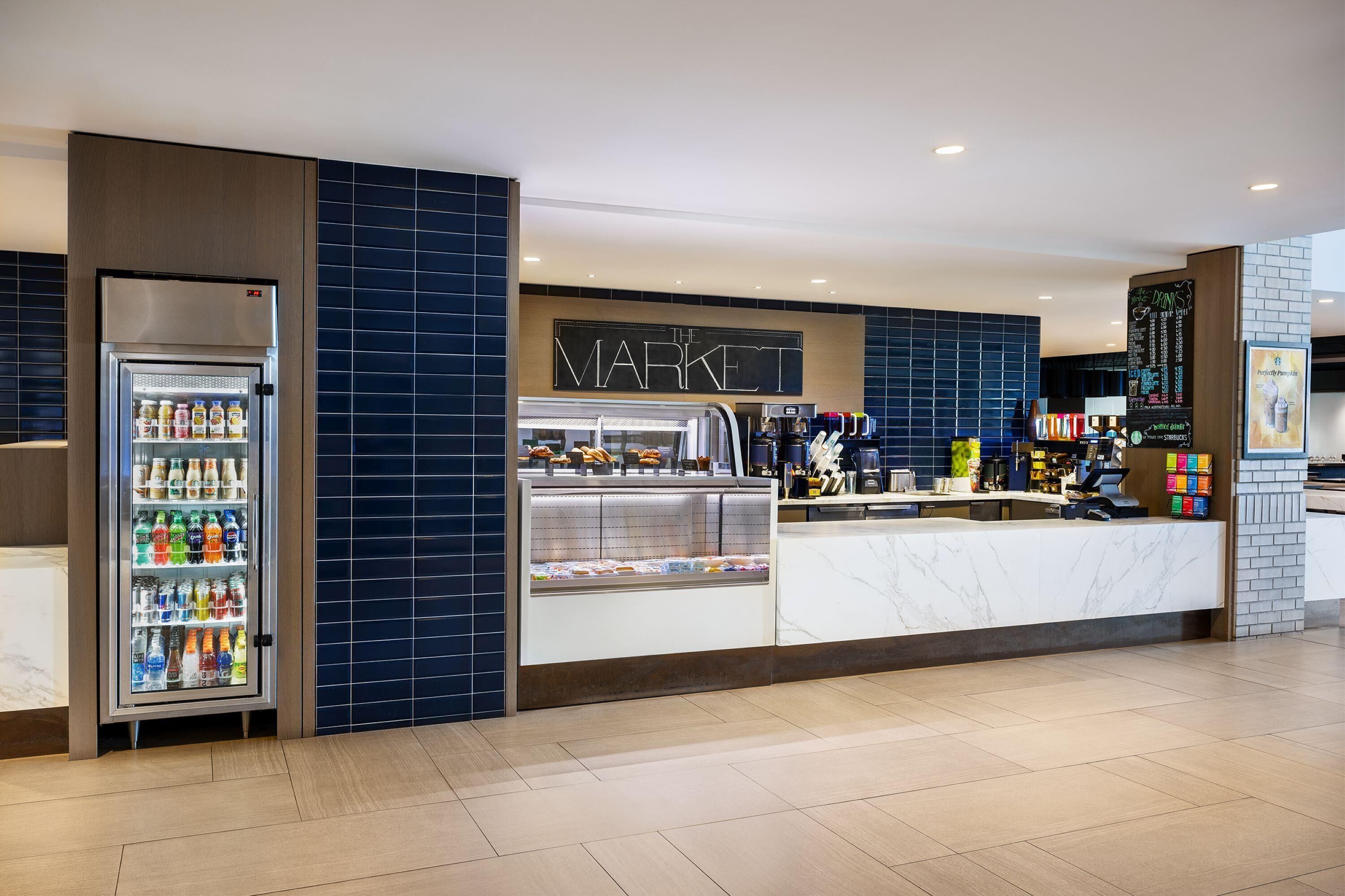 Un quiosco moderno con mostrador refrigerado y estación de café, identificado como 'THE MARKET'.