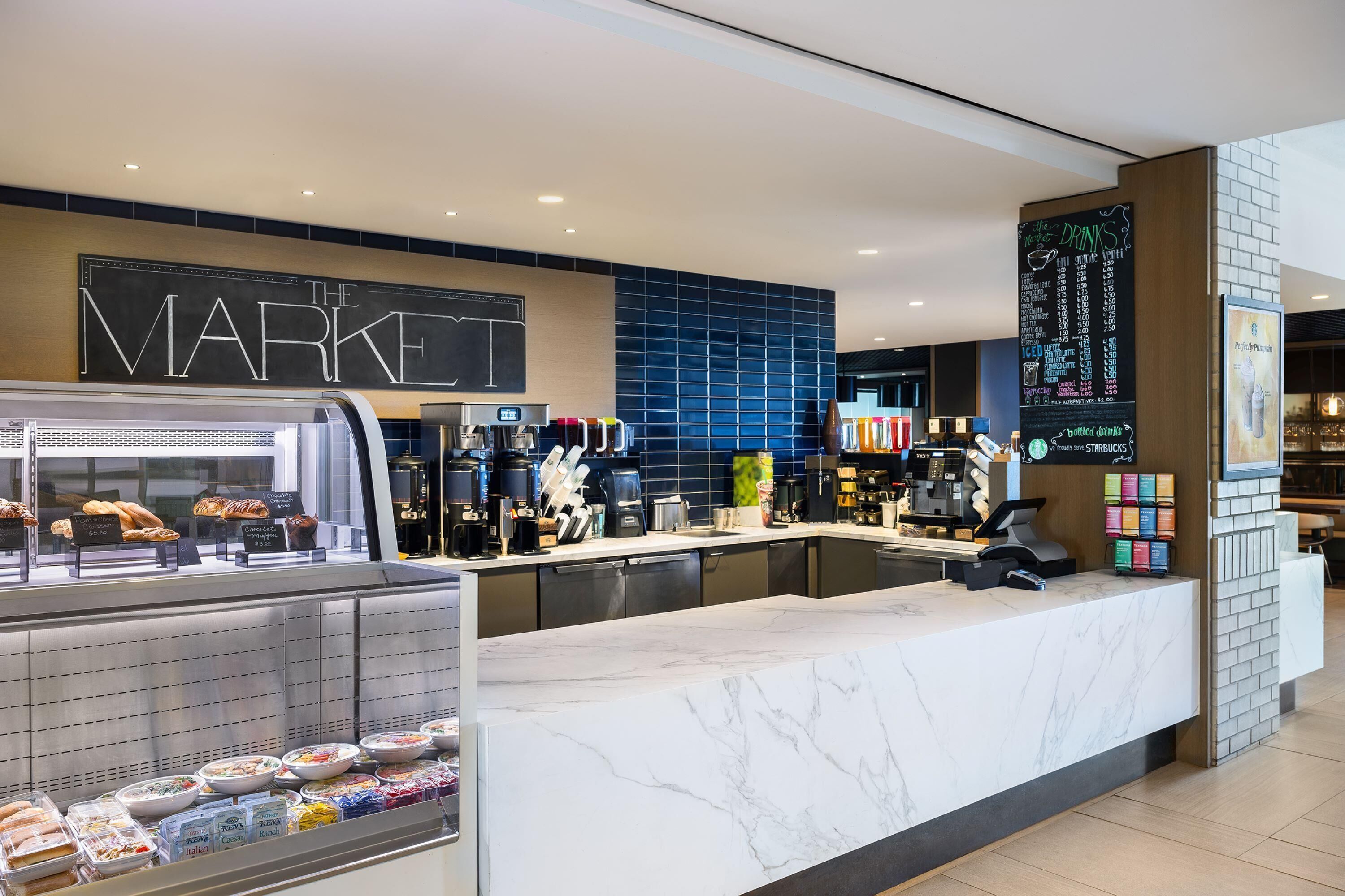 A modern coffee shop with a marble counter, a chalkboard menu, and a variety of baked goods and beverages displayed.