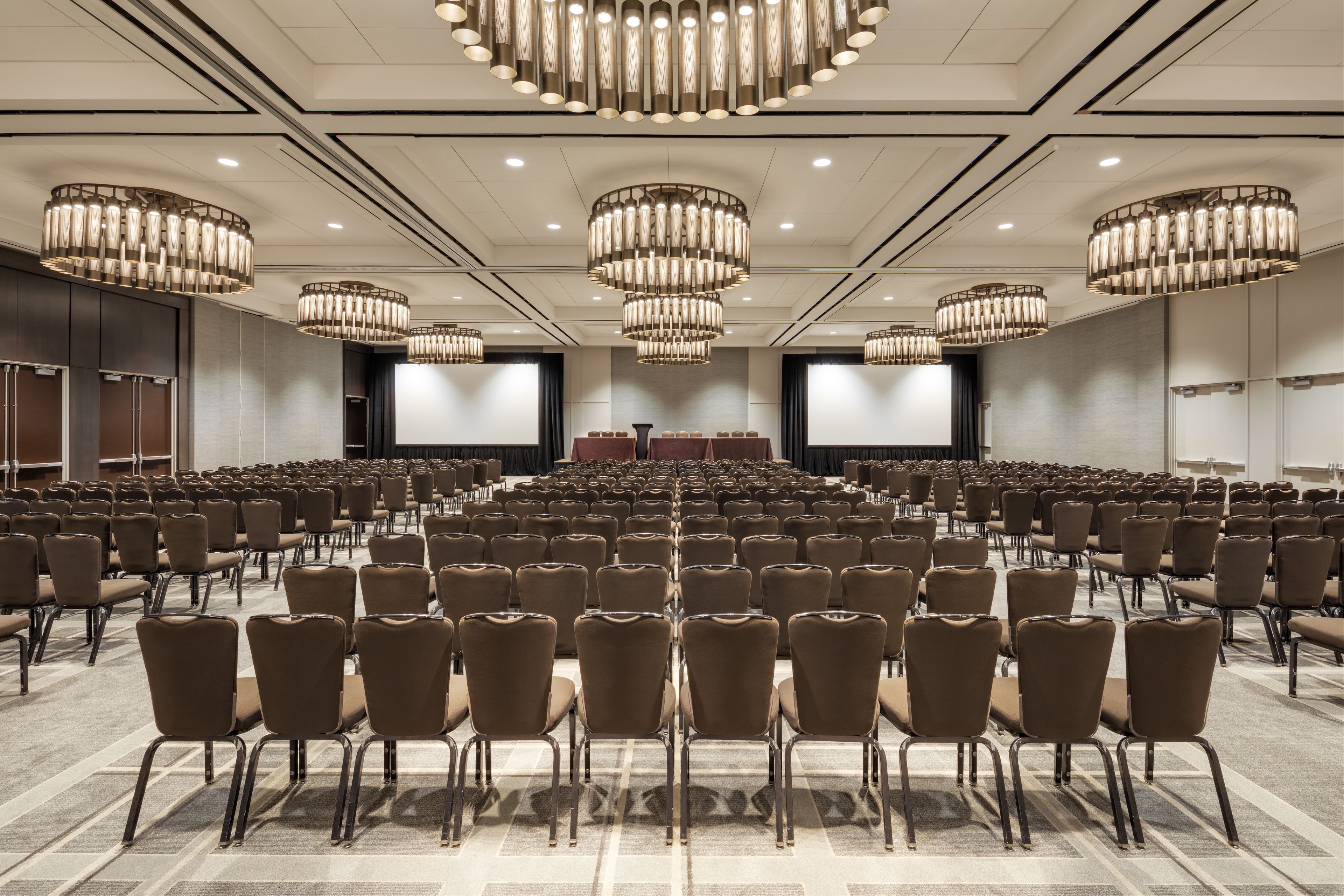 A large conference room with rows of chairs, a stage, and multiple chandeliers.