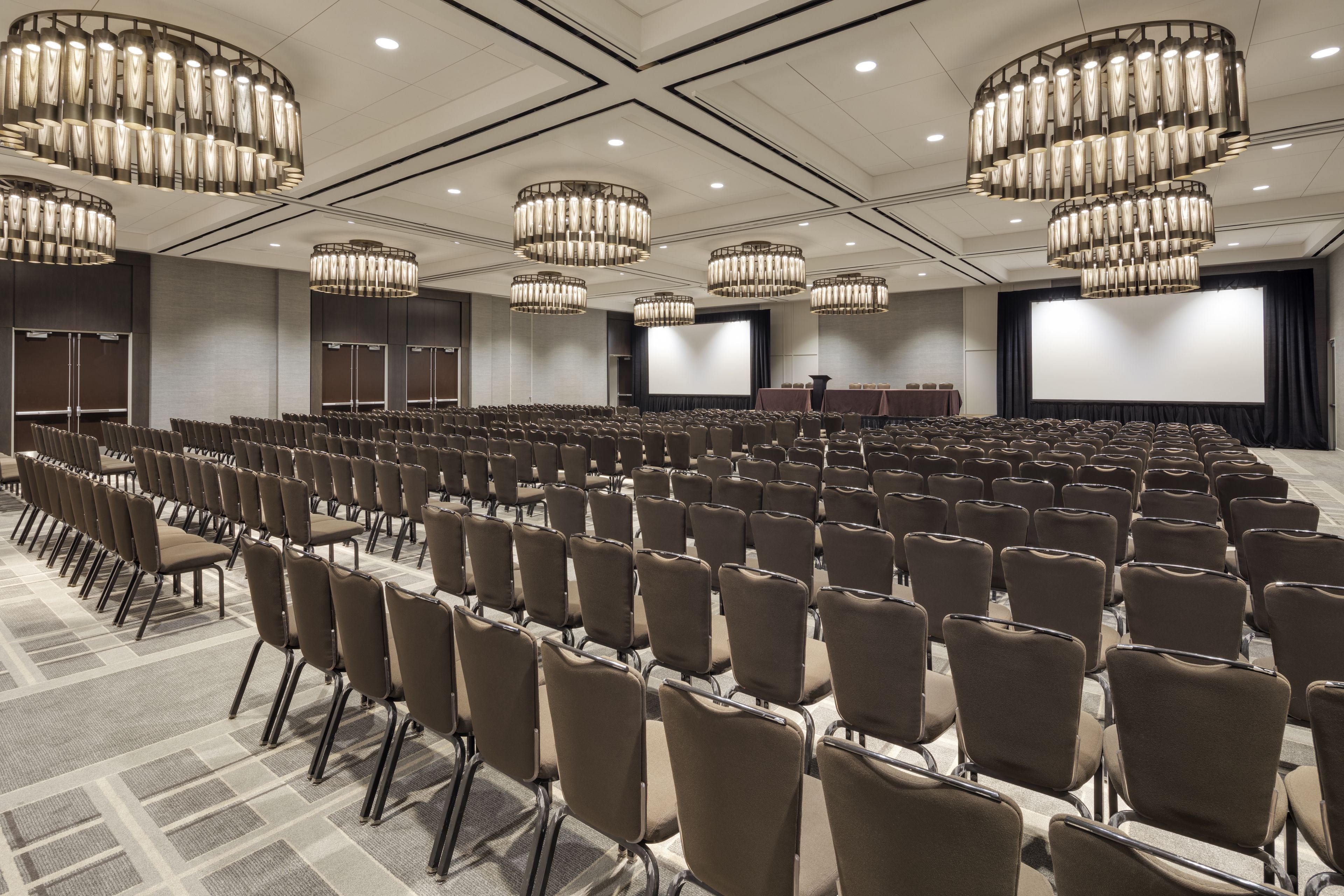 A conference room with rows of chairs, a large screen, and multiple chandeliers.