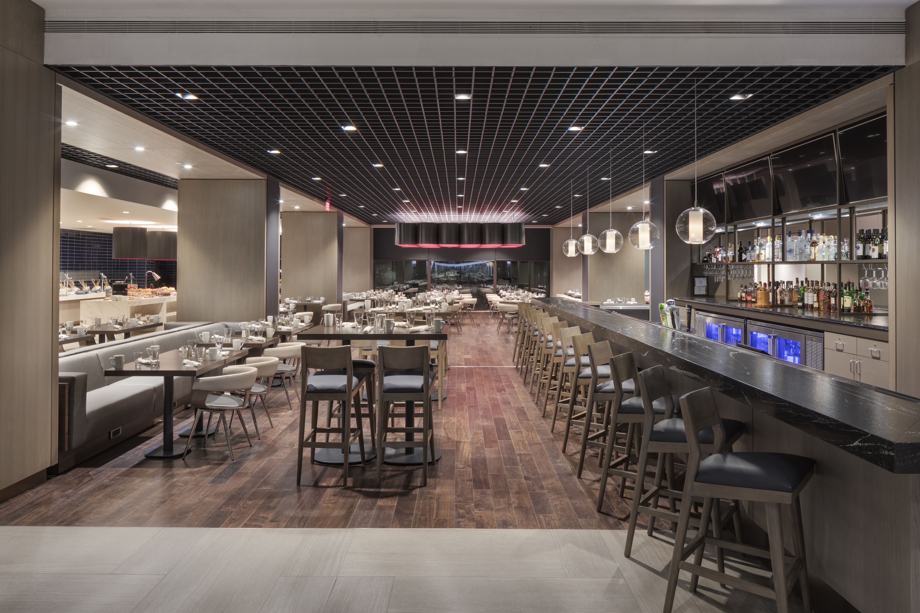 A modern restaurant with a long counter, multiple seating areas, and a bar with a variety of bottles.