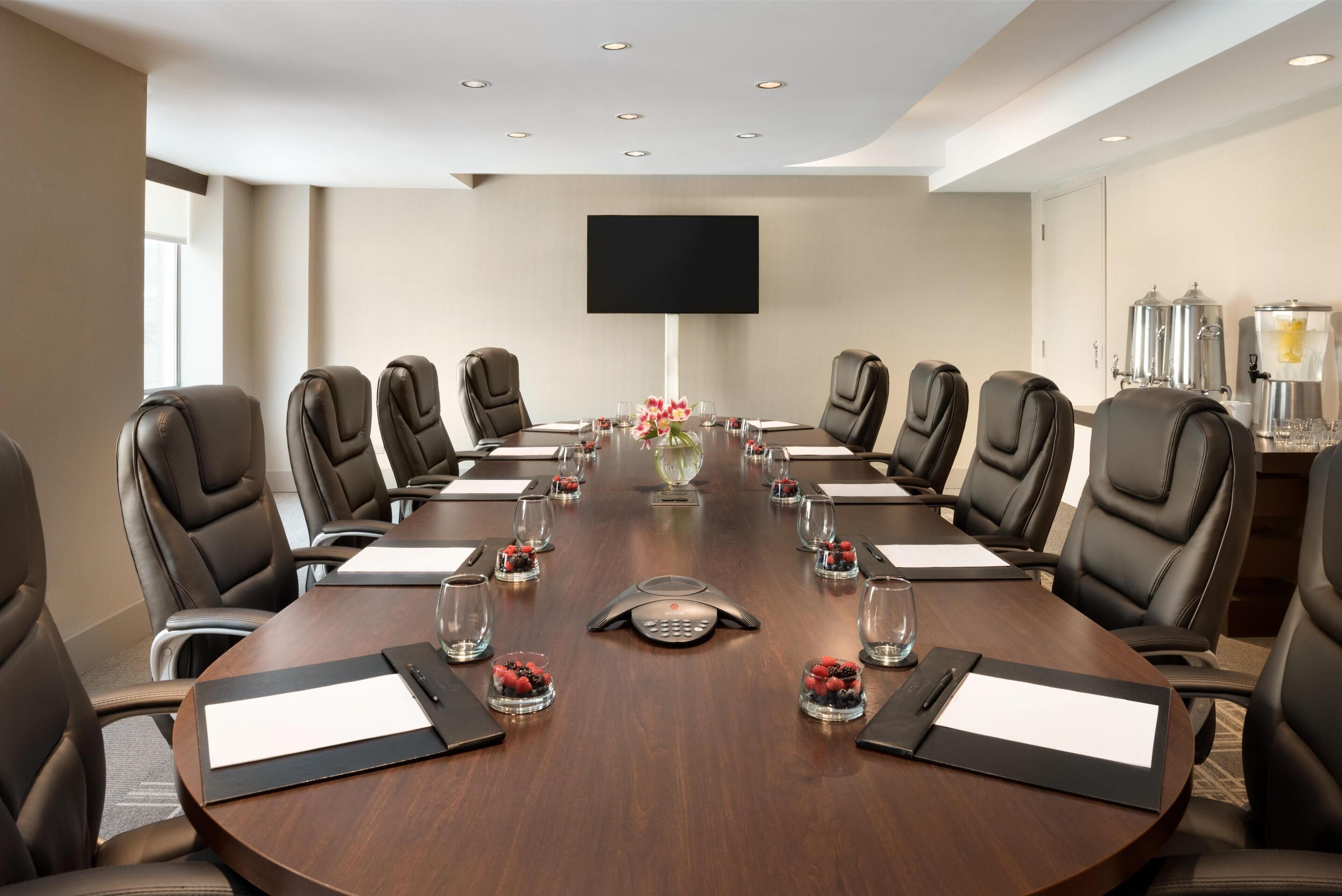 A conference room with a round table, black leather chairs, a flat-screen TV, and a coffee station.