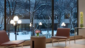 A modern interior with two chairs, a round table with a vase, and a large window offering a view of a snow-covered outdoor area with trees and a building. - Hyatt Regency Schaumburg Chicago (Schaumburg)