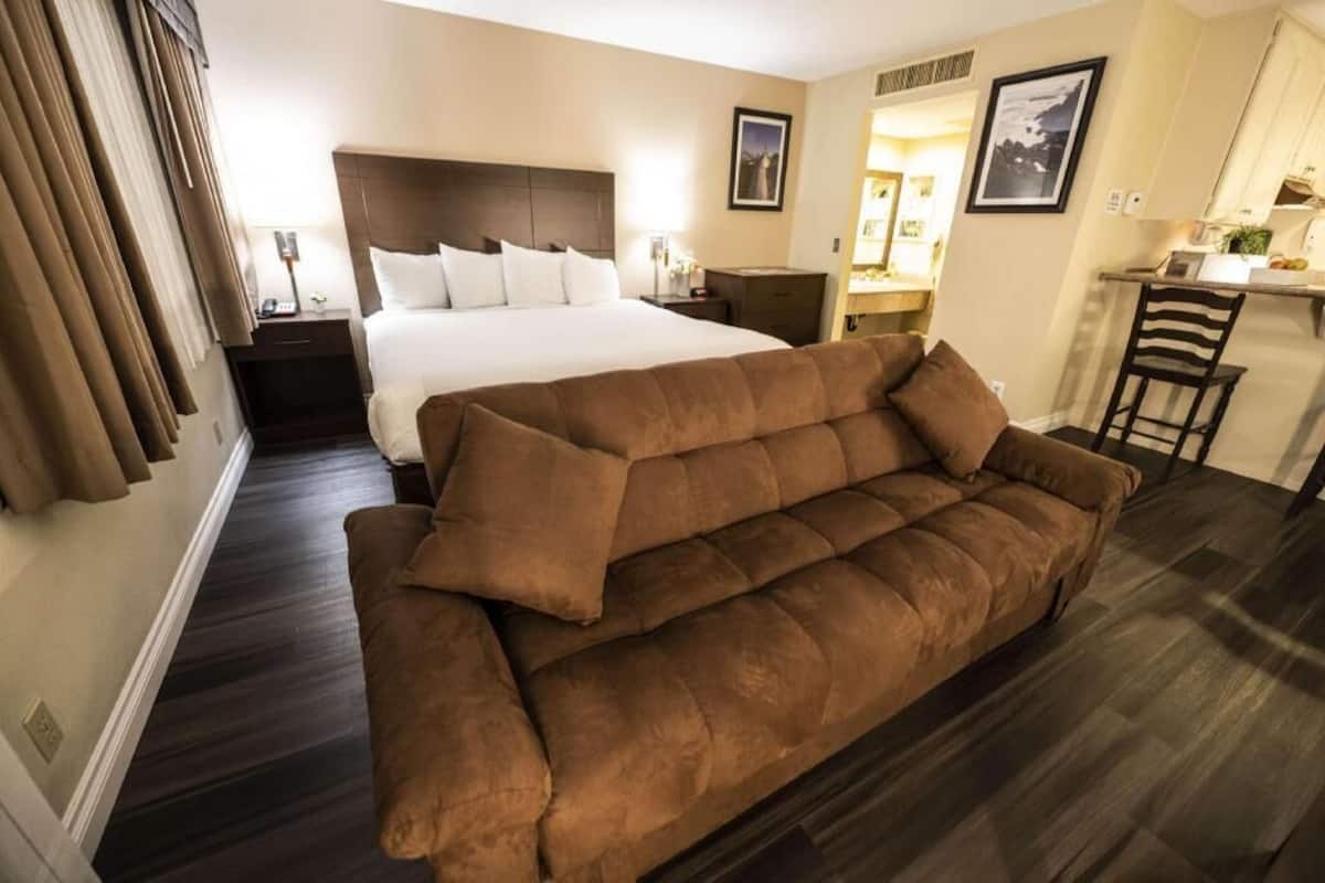 A hotel room with a large bed, a brown sofa, a desk, and a chair.