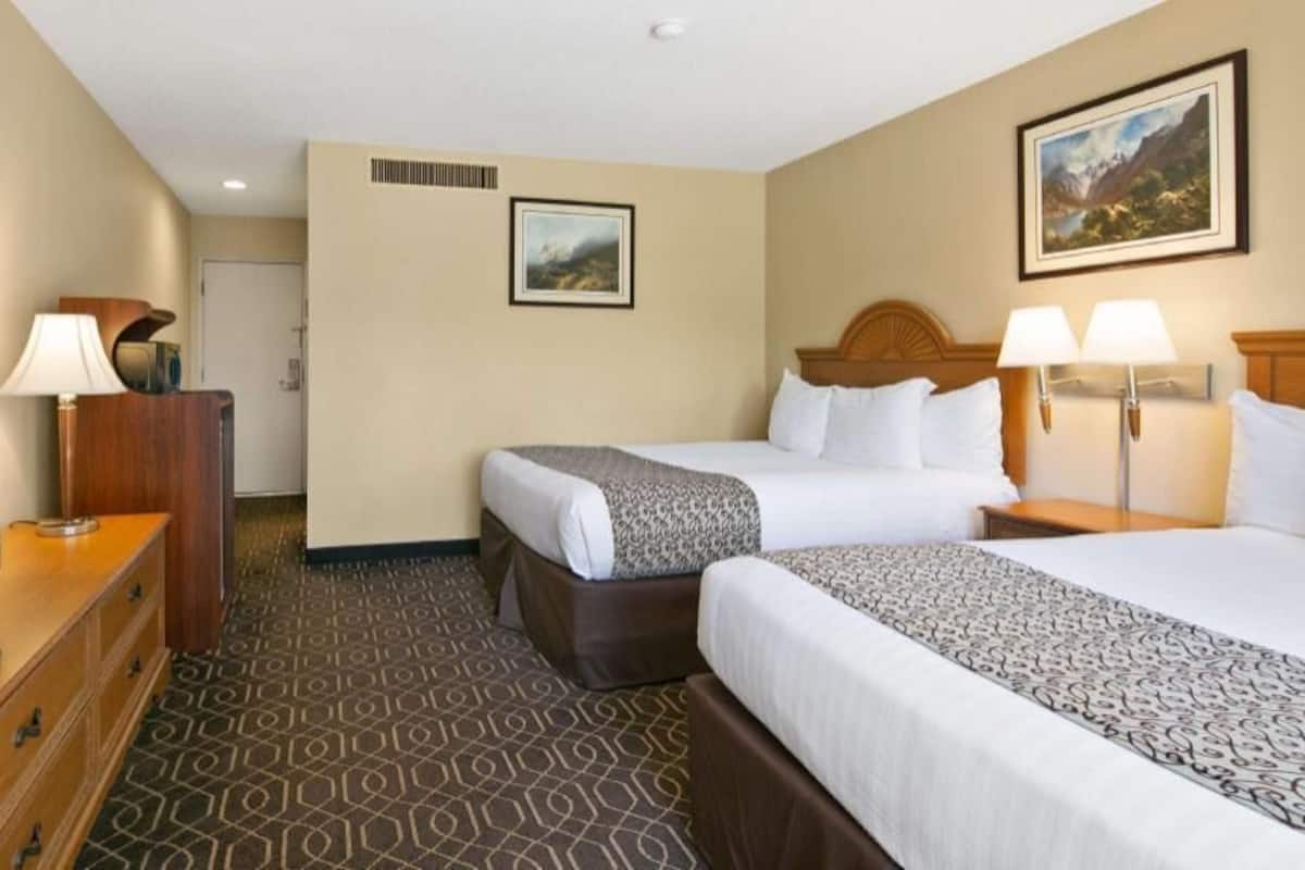 A hotel room with two beds, a TV, a dresser, and a painting on the wall.