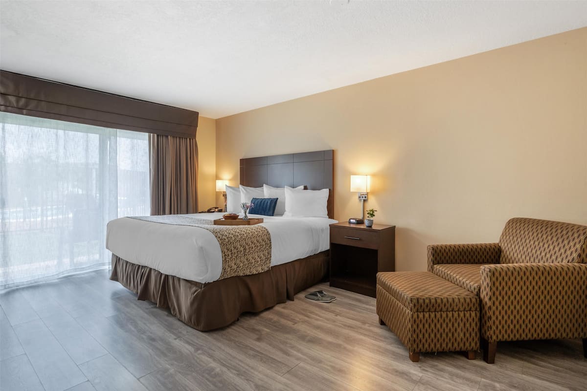 A hotel room with a large bed, two bedside tables with lamps, a chair, and a view of the outdoors.