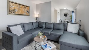 A modern living room with a grey sectional sofa, a small round coffee table, and a painting on the wall. - Best Western Westminster Inn (Westminster)