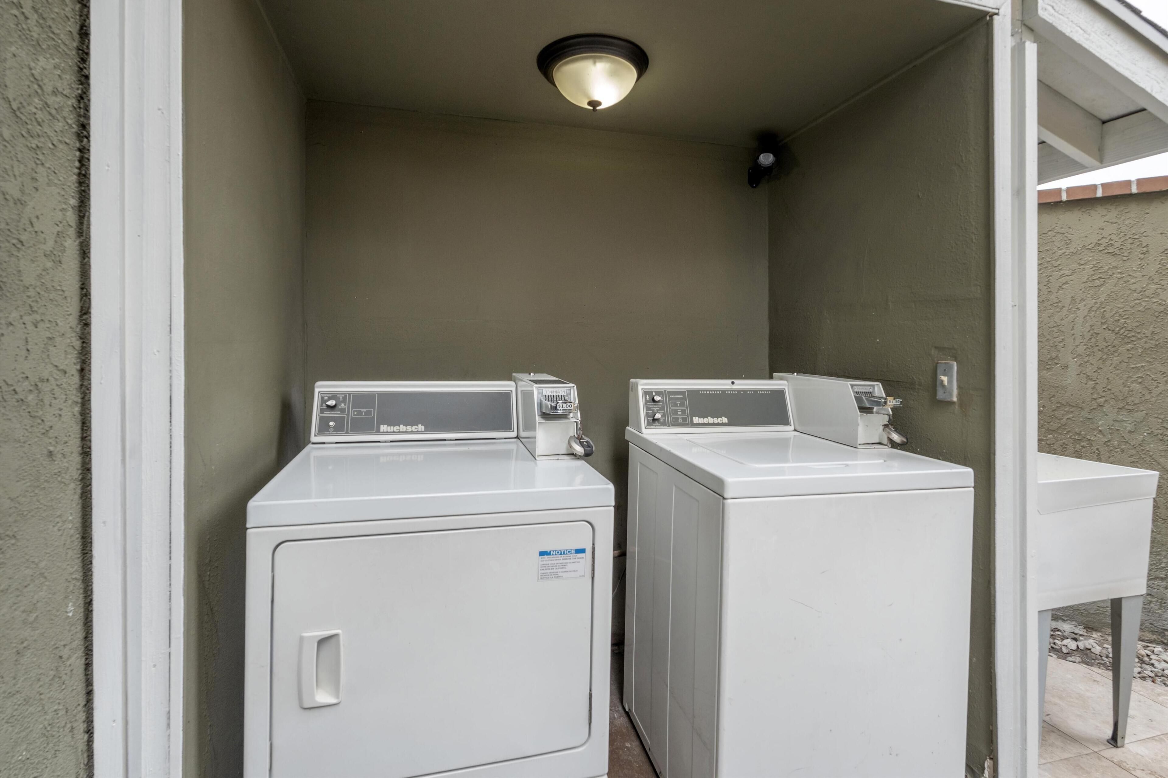 A laundry room with two front-loading washing machines, a white sink, and a light fixture on the ceiling.
