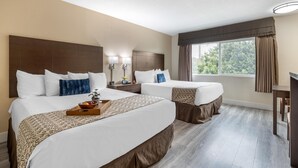 A hotel room with two beds, a wooden headboard, a bedside table with lamps, a window with curtains, and a view of greenery outside. - Best Western Westminster Inn (Westminster)