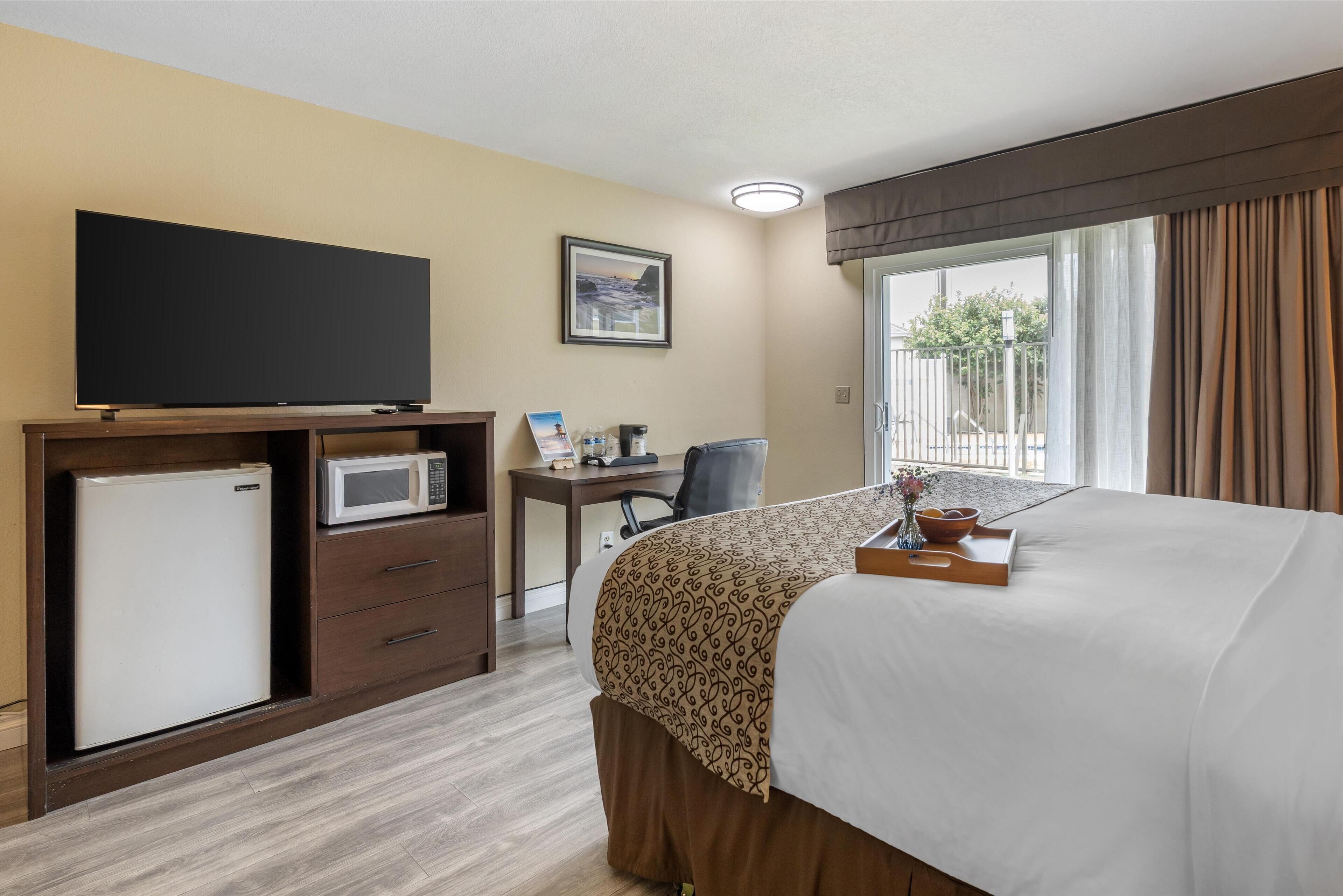A hotel room with a bed, a desk with a computer, a TV, a microwave, and a refrigerator.