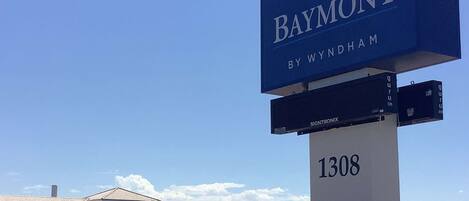 A Baymont by Wyndham hotel sign with a clear sky and a building in the background.