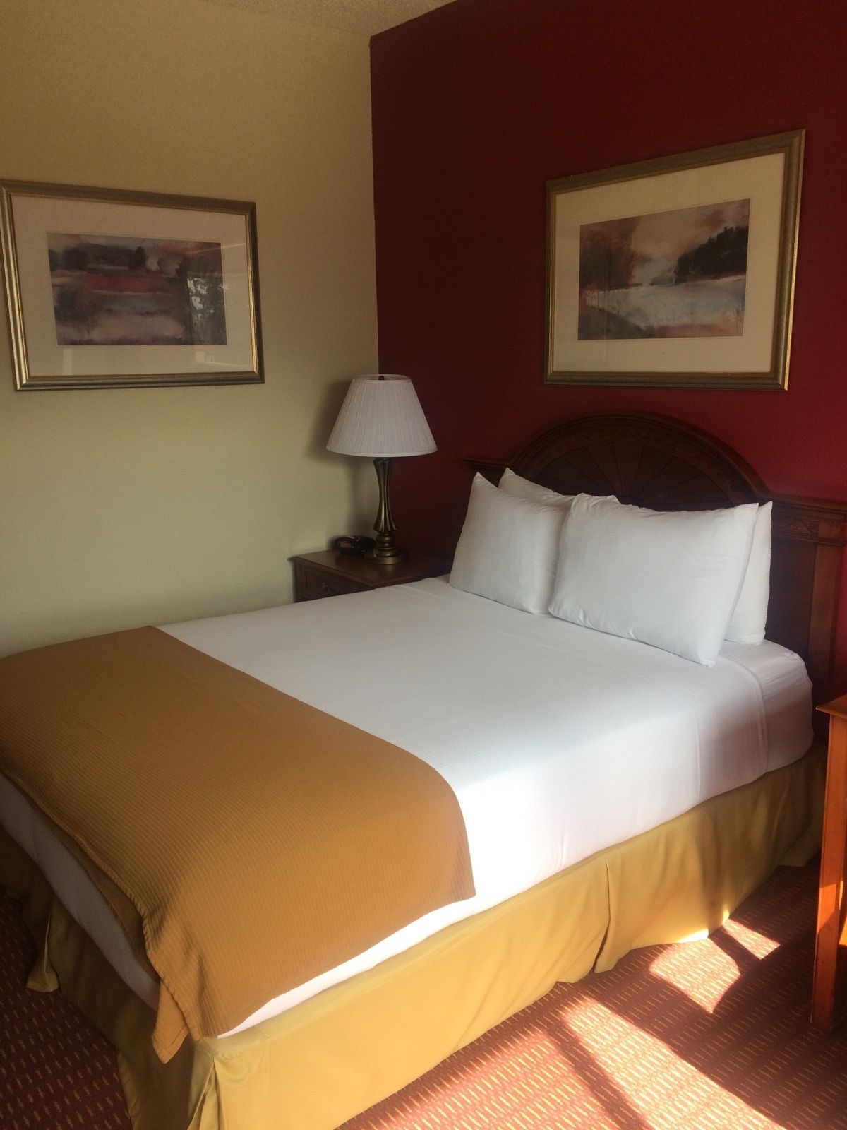 A neatly made bed with white linens and a brown throw blanket, a bedside lamp, and two framed pictures on the wall.