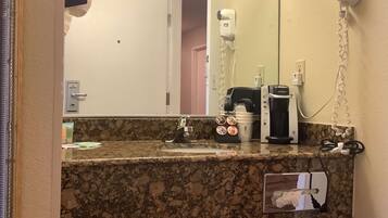 Ein Badezimmer mit Granitplatte, einem Spiegel, einem Föhn, einer Kaffeemaschine und einem Handtuchspender.
