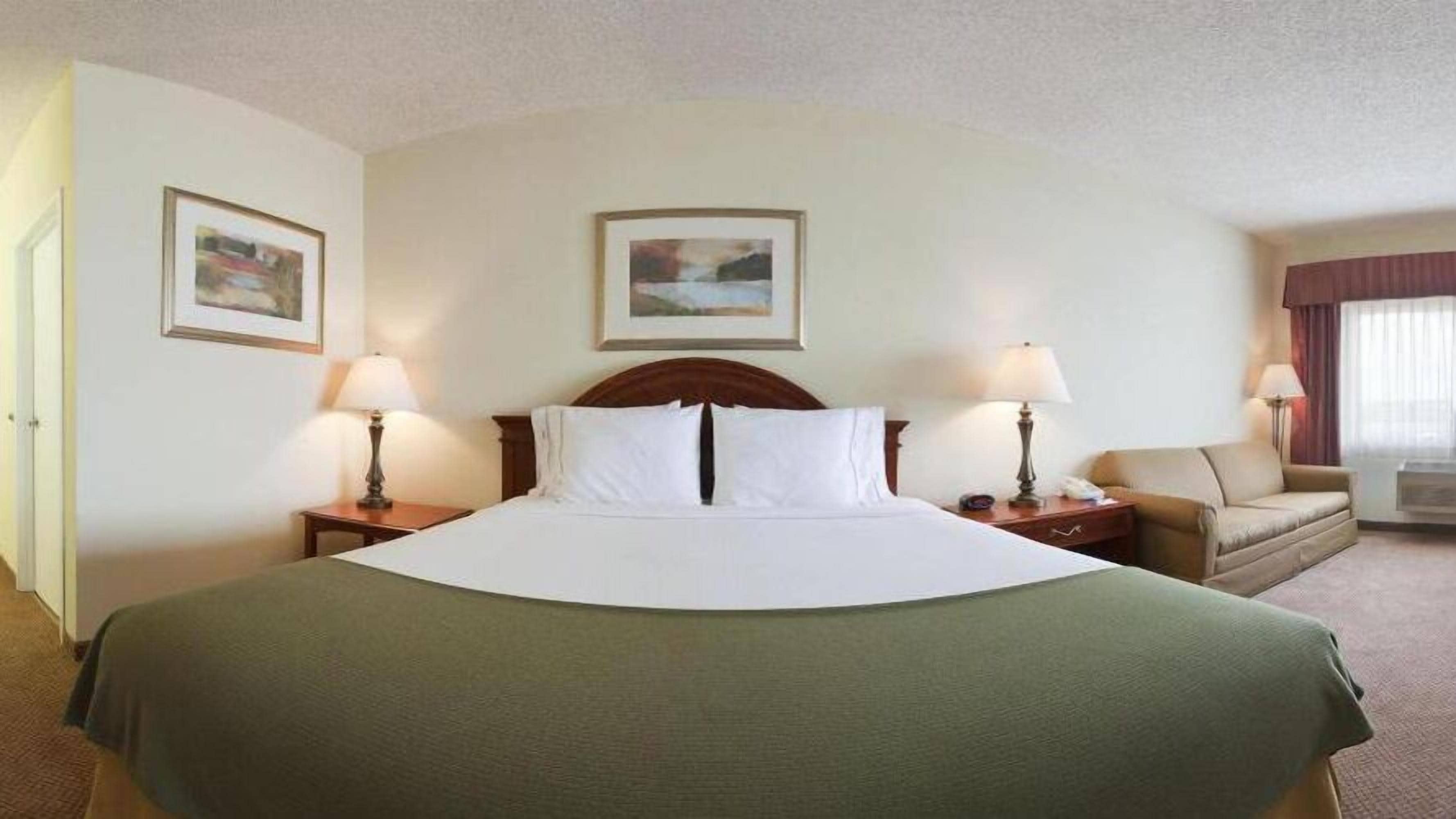 A hotel room with a large bed, two bedside tables with lamps, a sofa, and two framed pictures on the walls.