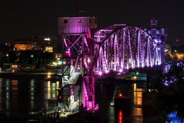Une vue nocturne d’un pont illuminé de lumière violette, d’une tour de contrôle et d’un paysage urbain en arrière-plan.