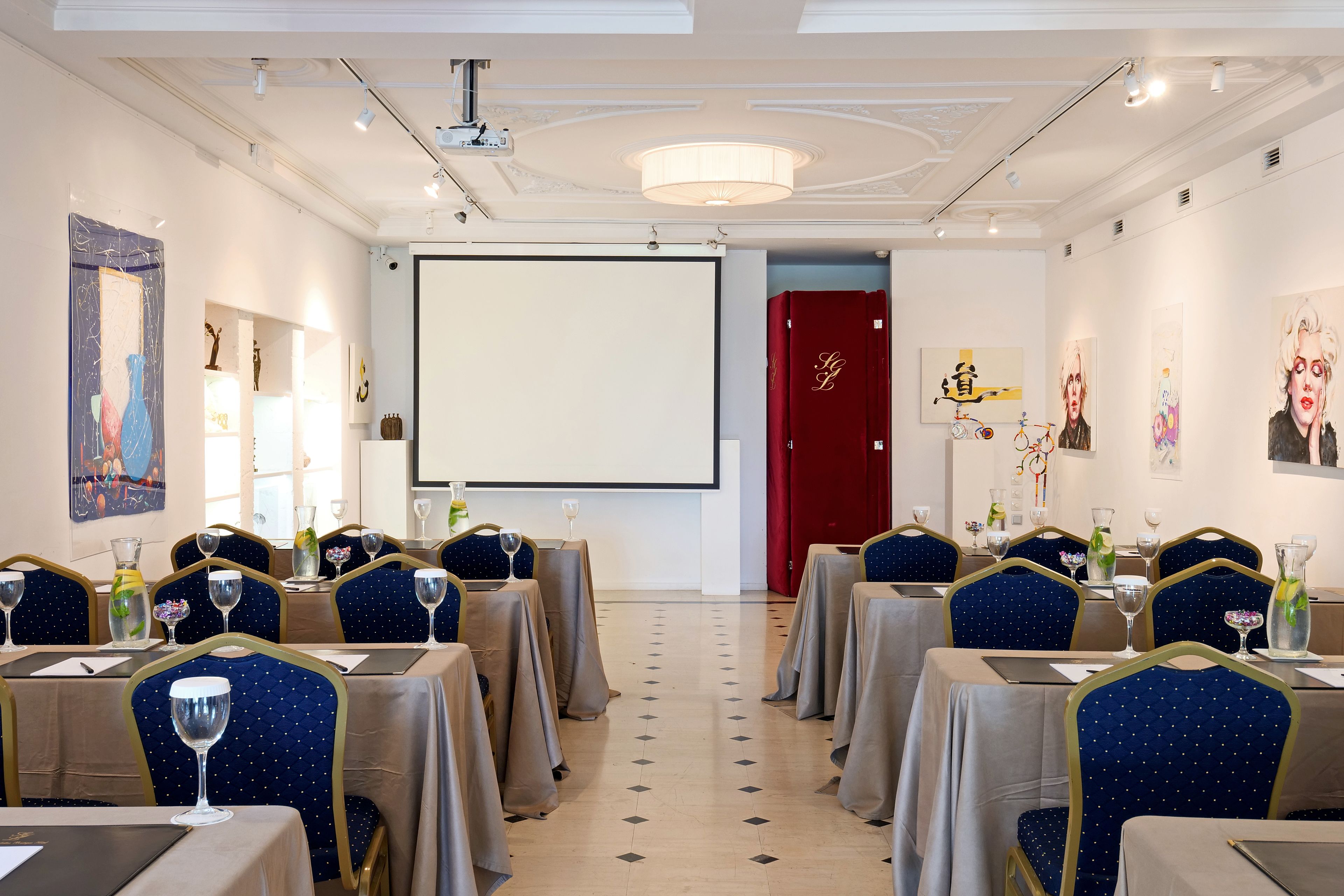 A conference room with tables set for a meeting, a projector screen, and artwork on the walls.