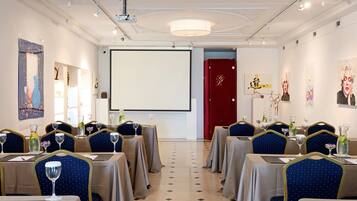 A conference room with tables set for a meeting, a projector screen, and artwork on the walls.