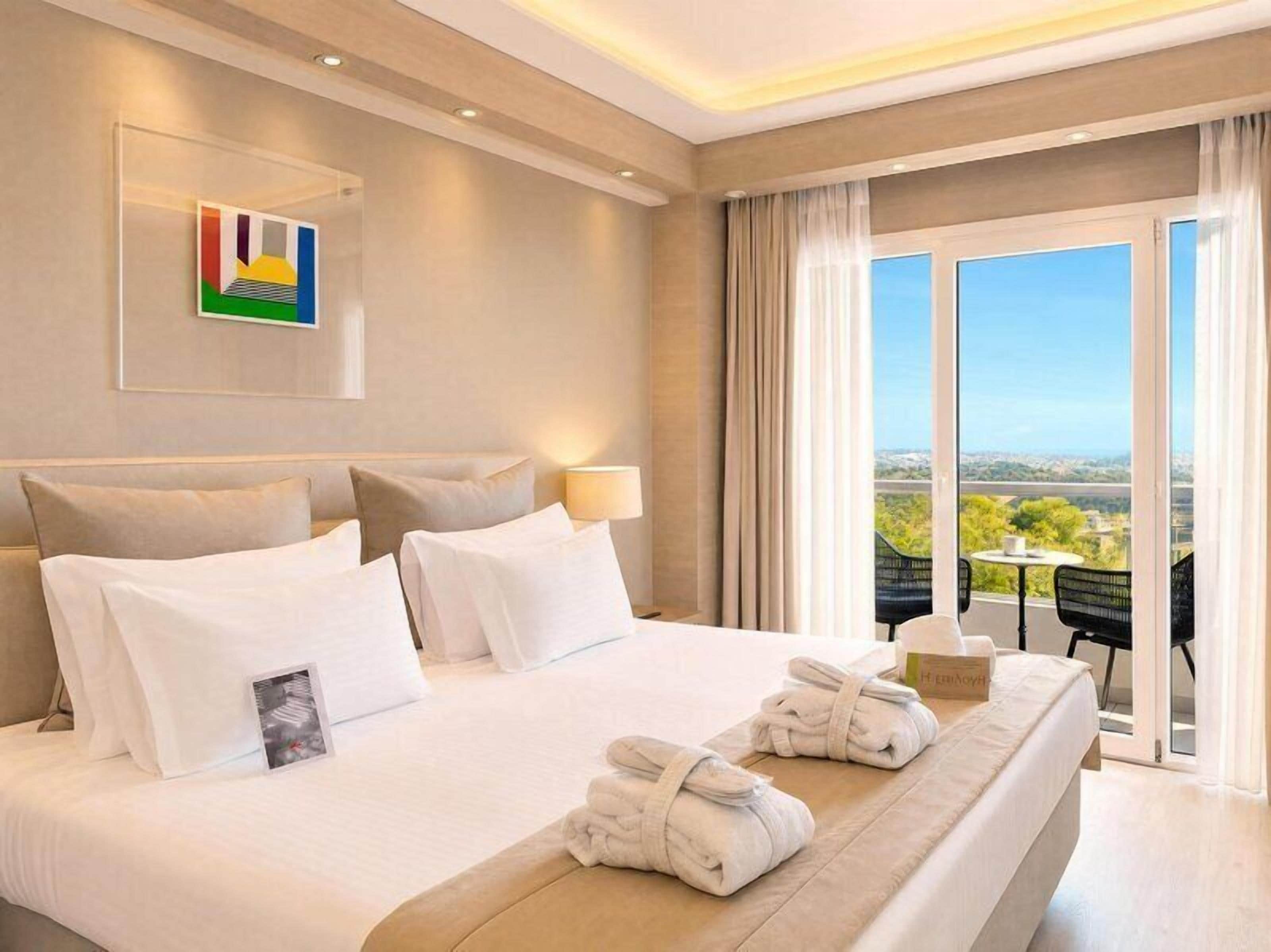A hotel room with a large bed, a view of the outdoors, and a balcony with chairs.