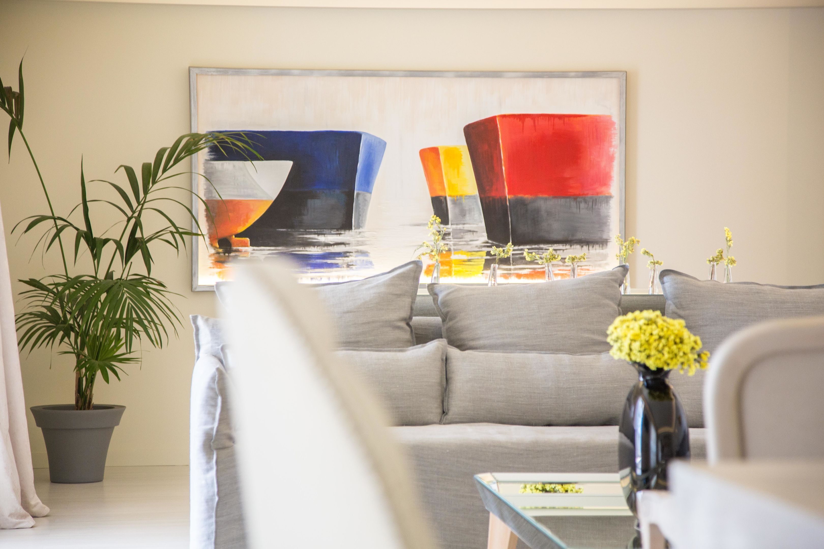 A modern living room with a grey sofa, a glass coffee table, and a painting on the wall.