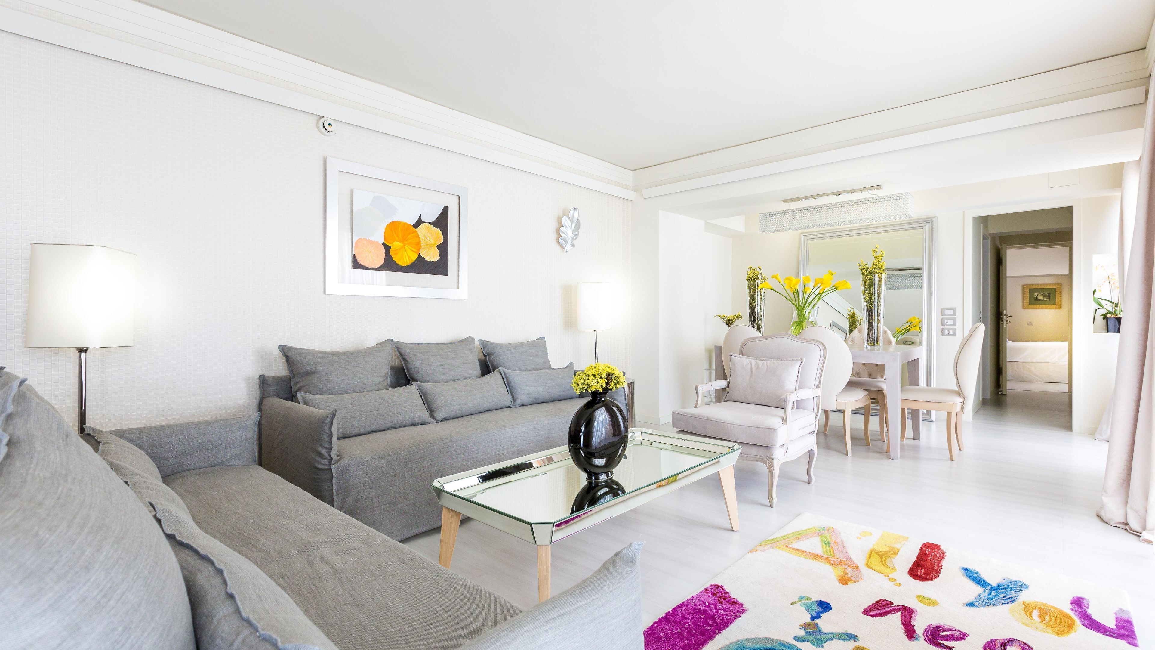 A modern living room with a grey sofa, a glass coffee table, and a colorful rug.
