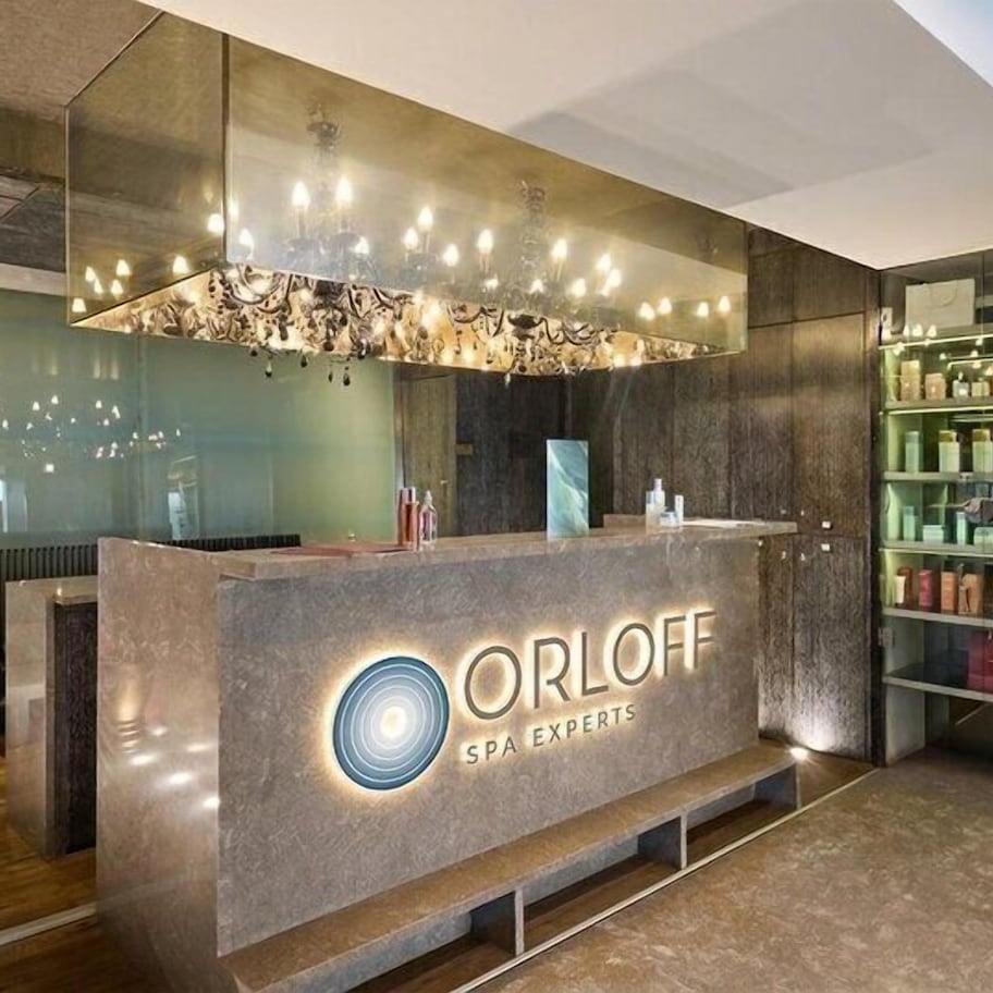 A reception desk with a modern design, a chandelier, and a display of products on shelves.