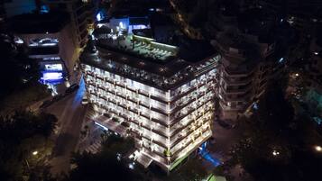 Ein mehrstöckiges Hotel mit Dachterrasse, mehreren Balkonen und einer gut beleuchteten Fassade.