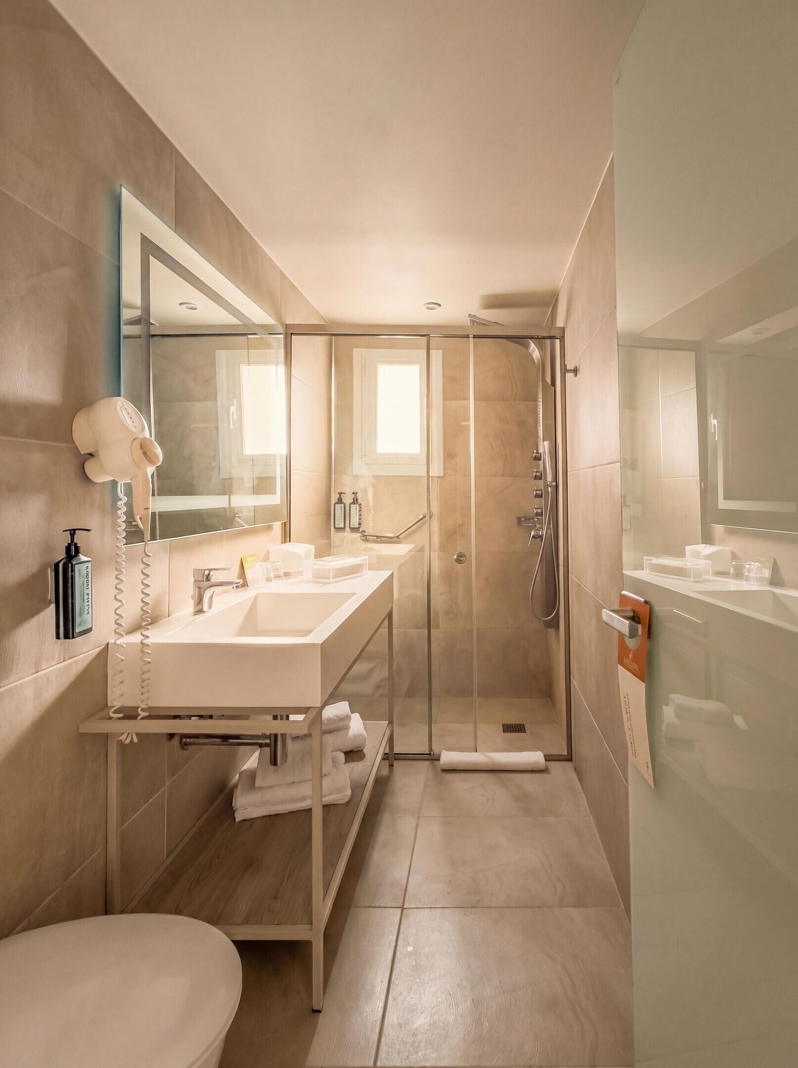 Une salle de bain moderne dotée d’une douche à parois de verre, d’un meuble-lavabo à deux vasques et d’un sèche-cheveux fixé au mur.