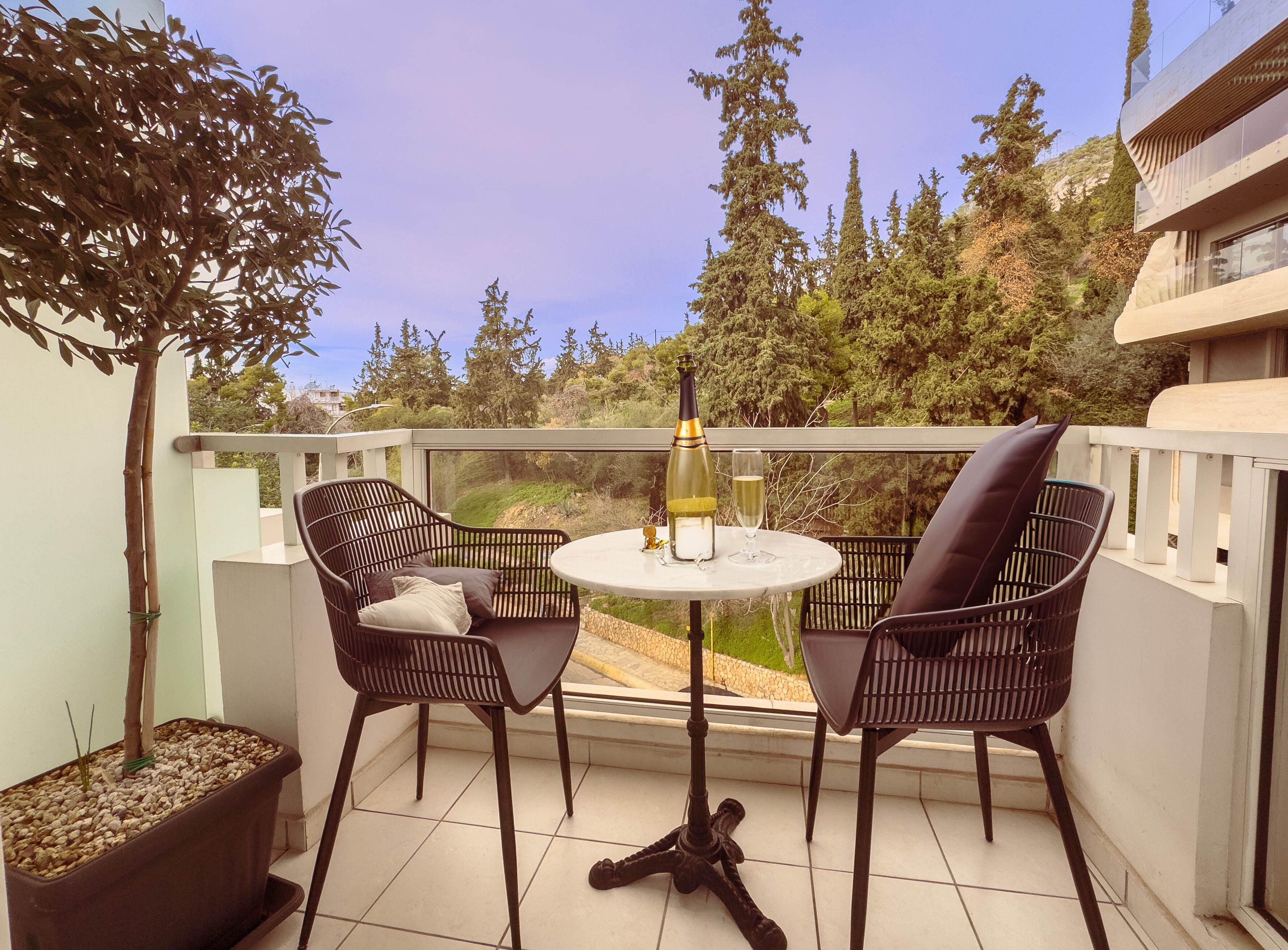 A balcony with two chairs, a table, a bottle of wine, and a glass.