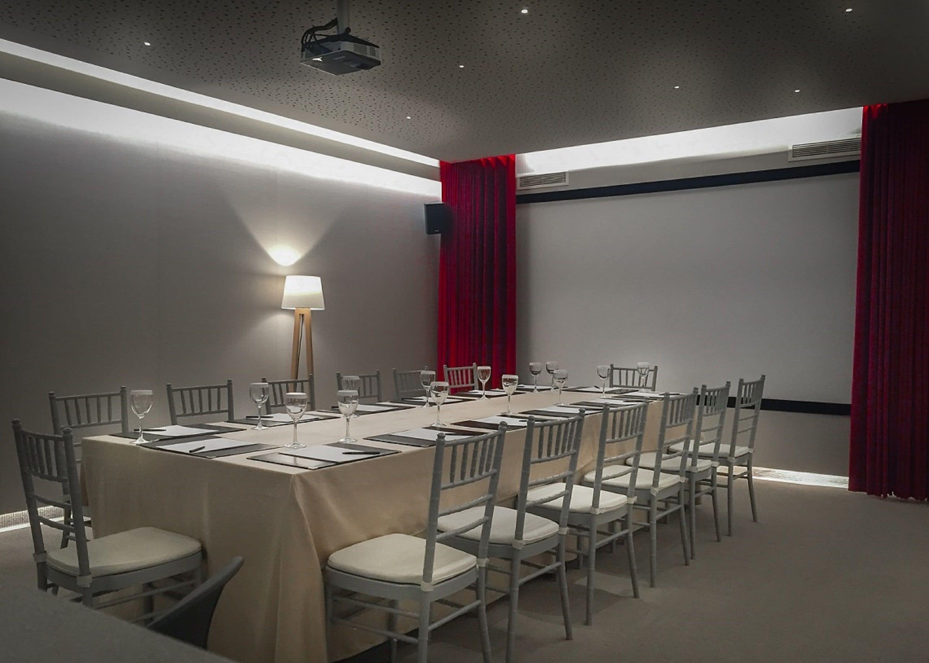A conference room with a long table, chairs, a projector, and a red curtain.