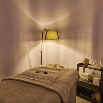 A room with a bed, a bedside table with toiletries, and a lamp.