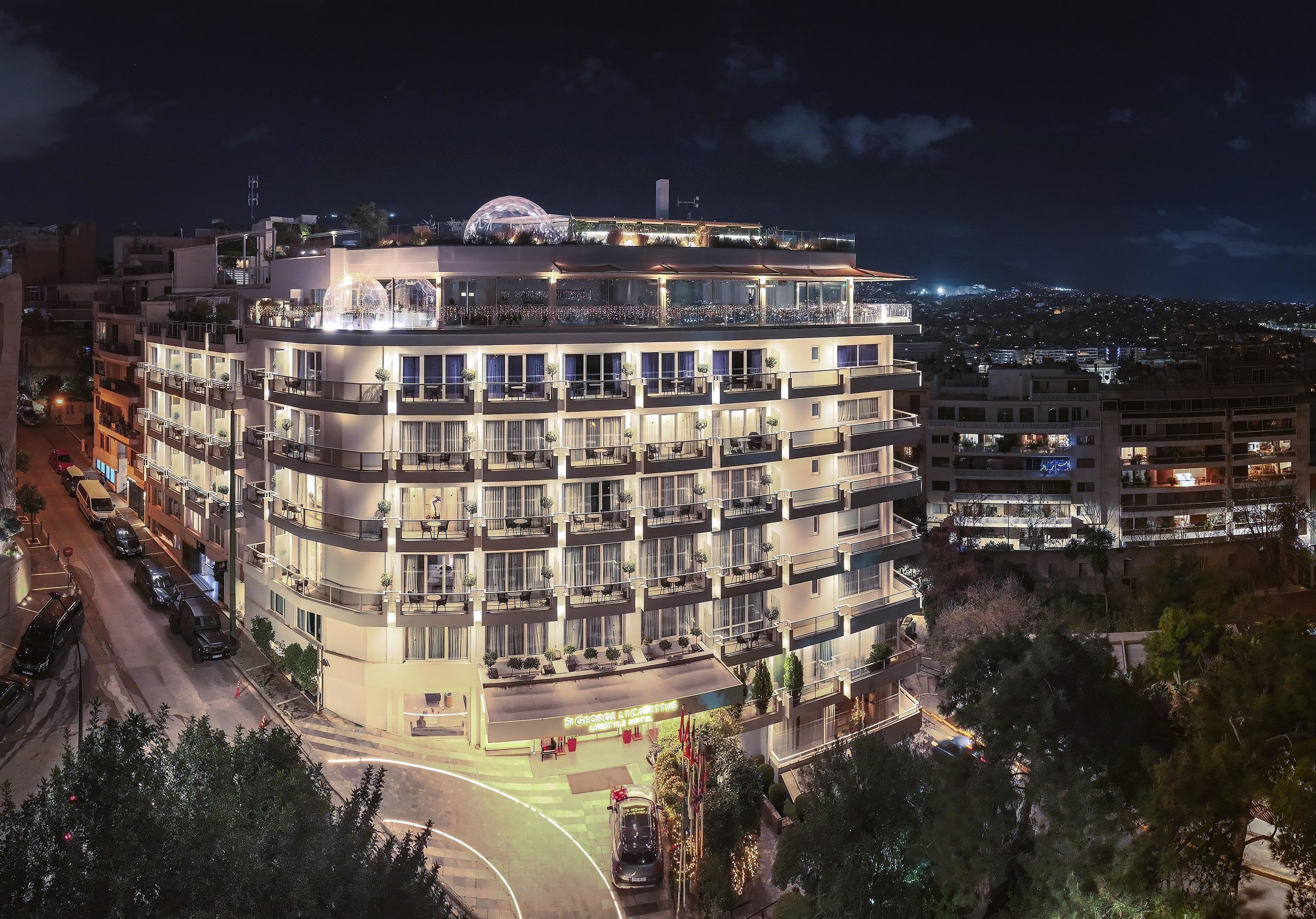 A multi-story hotel with balconies, a rooftop terrace, and a parking area.