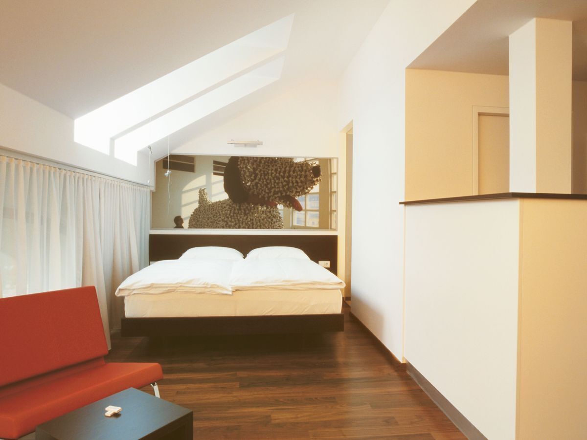 Un dormitorio con cama, un sofá rojo, una mesita y un tragaluz.