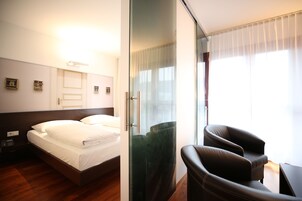 Habitación de hotel con cama, una silla, una mampara de vidrio y vistas al exterior.