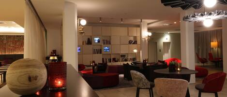 A modern living room with a dark wooden bar, red and black seating, and a TV in the background.