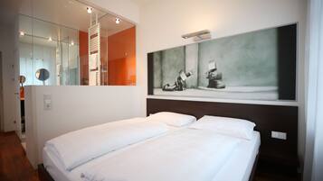 A hotel room with a large bed, a mirror, and a painting on the wall.