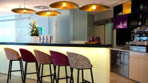 A modern kitchen with a bar area, featuring a long counter with bar stools, a refrigerator, and a wine cooler. - arte Hotel Linz (Linz)