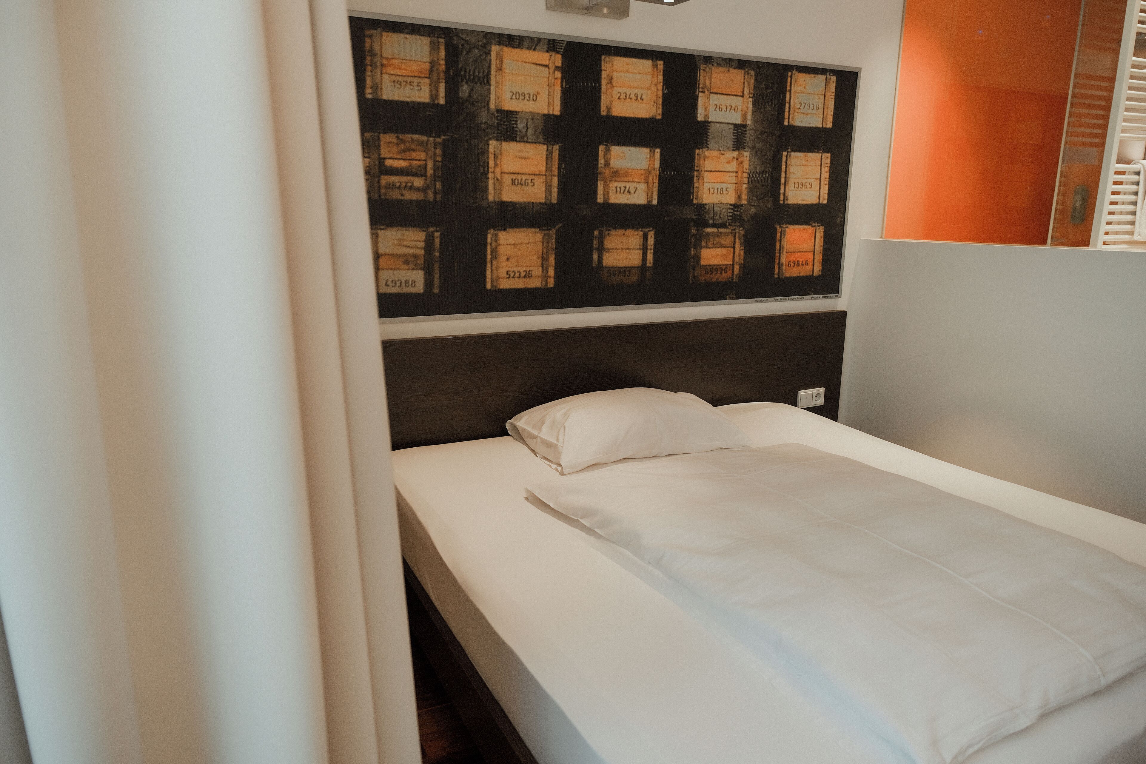 A single bed with white bedding, a headboard with a black panel, and a wall with numbered boxes.