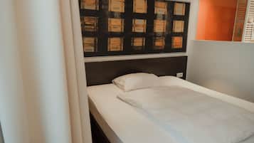 A single bed with white bedding, a headboard with a black panel, and a wall with numbered boxes.