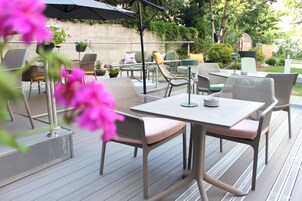 Un patio al aire libre con mobiliario de metal, incluyendo mesas y sillas, y una pérgola que proporciona sombra.