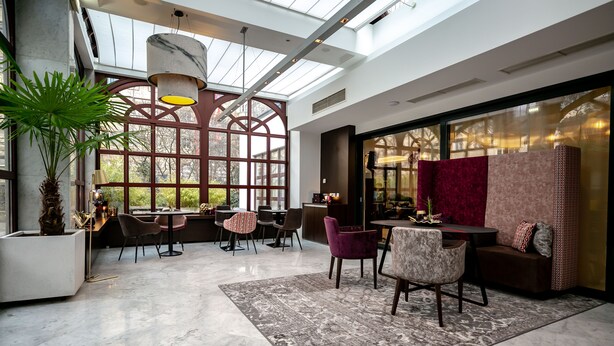 A spacious interior with a high ceiling, large windows, and a mix of seating areas including a bar and a dining area. - arte Hotel Linz (Linz)