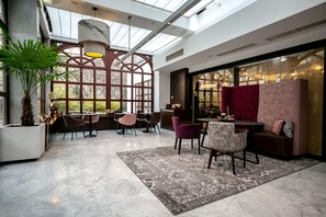 Un interior amplio con techo alto, ventanas grandes y una combinación de espacios para sentarse, incluyendo un bar y una zona de comedor.