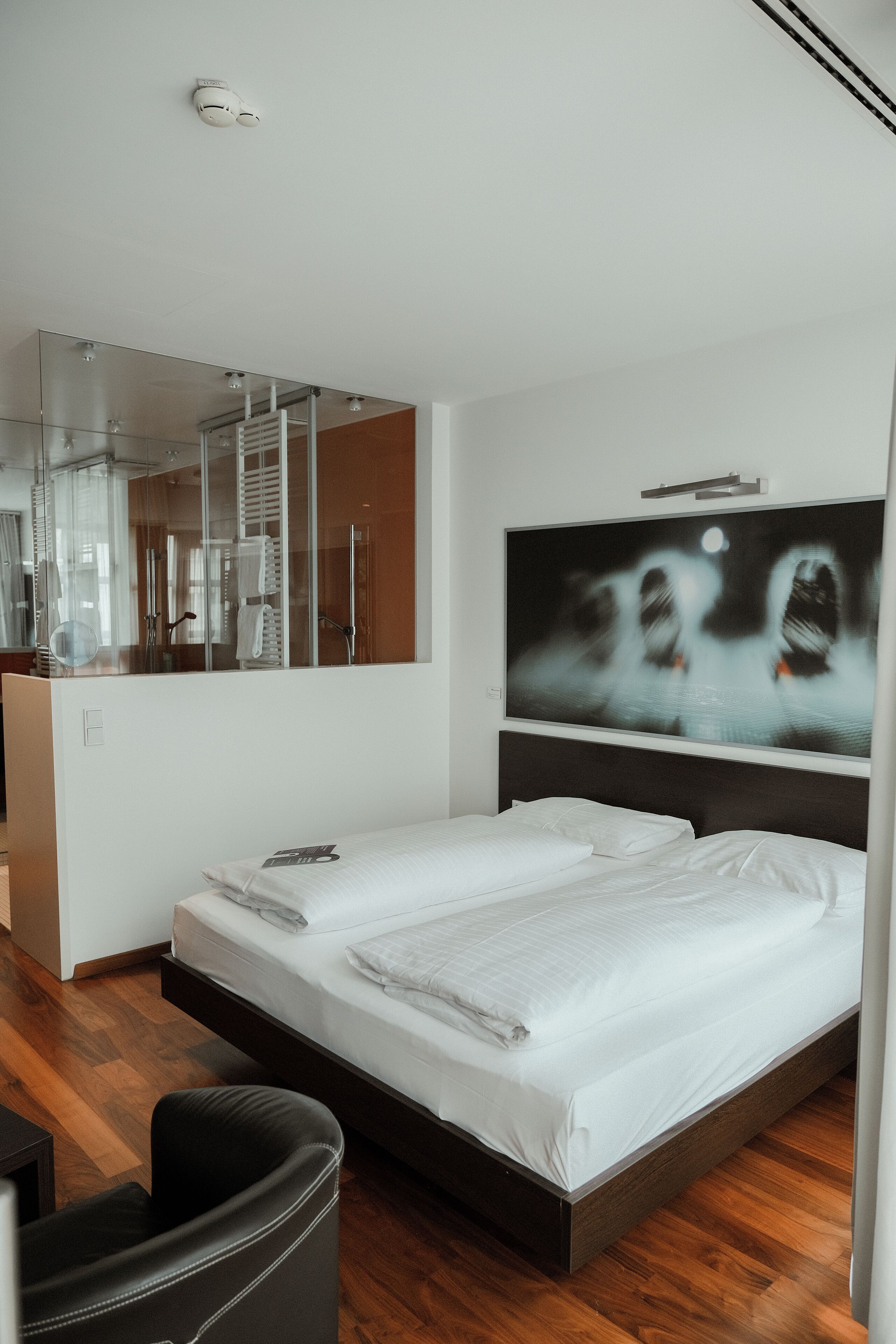 A modern hotel room with a large bed, a seating area, a large mirror, and a wall-mounted TV.