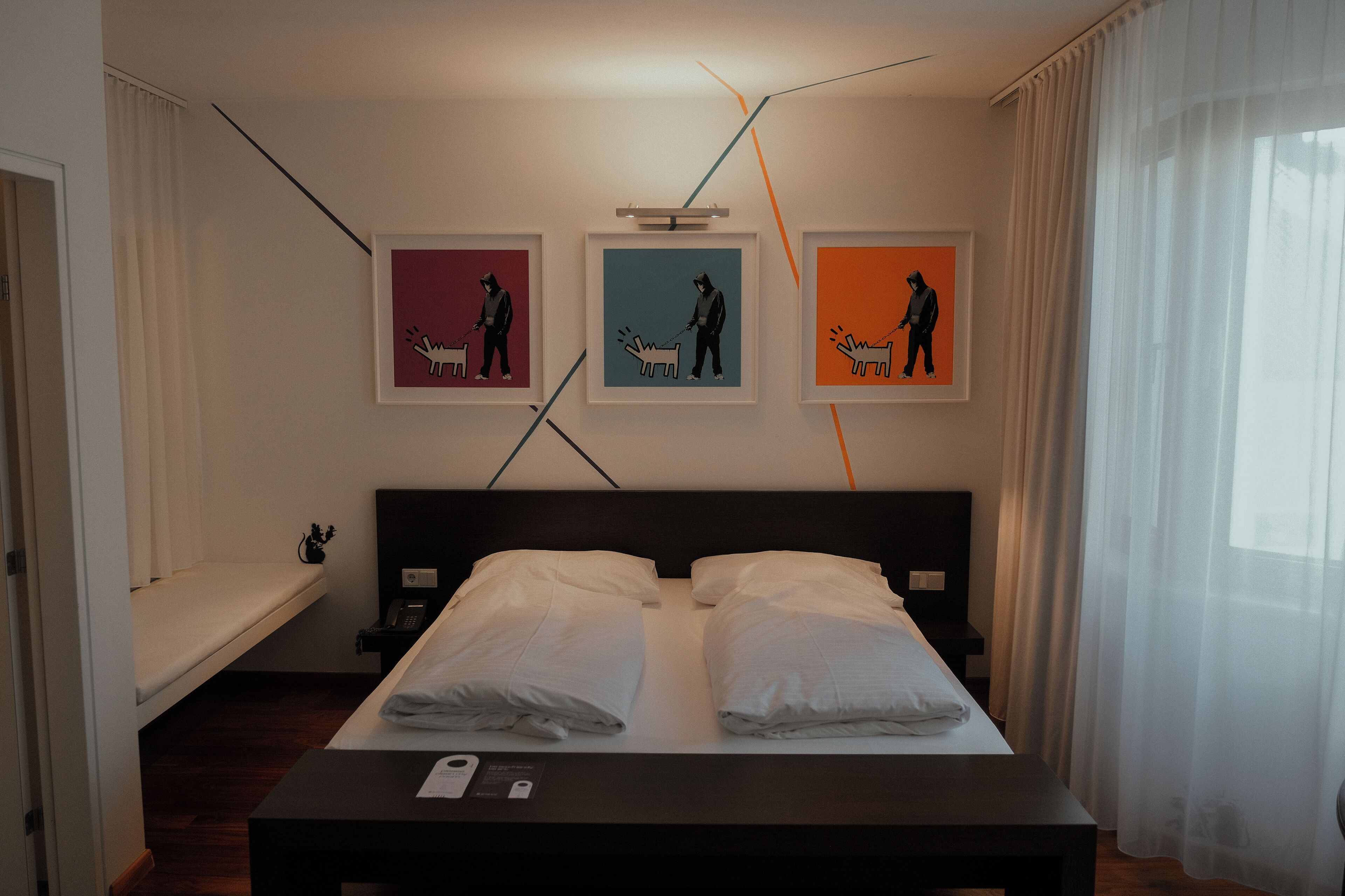 Habitación de hotel con una cama, una mesita de noche con teléfono y tres cuadros en la pared.