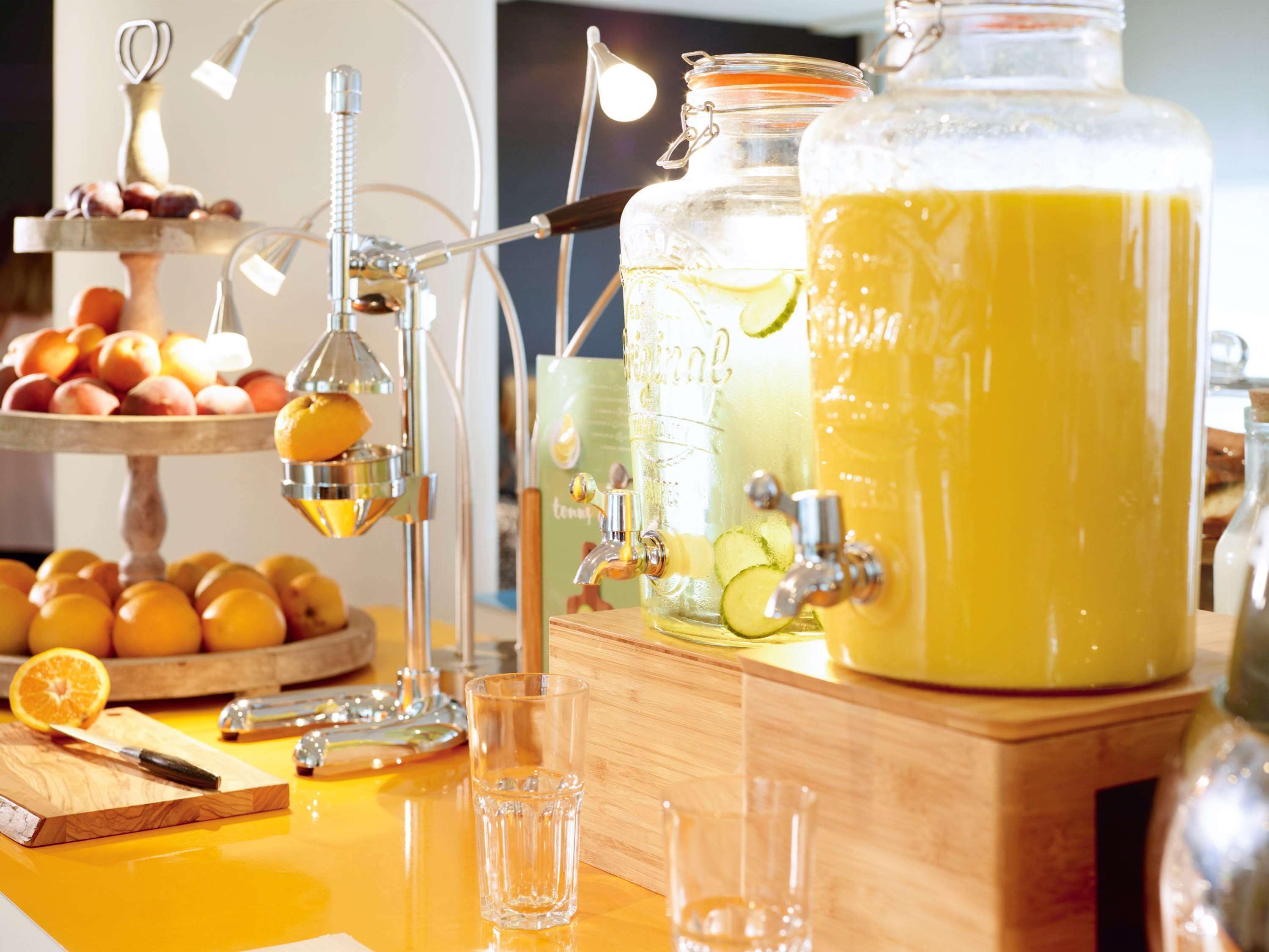 Uma estação de bebidas com espremedor, uma grande tigela de ponche e uma exposição de frutas.