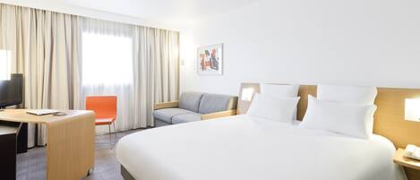 A hotel room with a large bed, a desk, a chair, and a television.